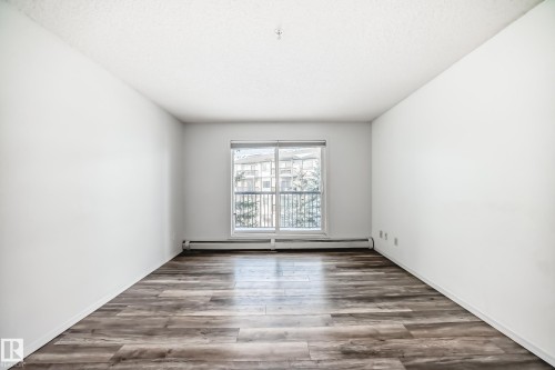 Empty room with wood finished floors, baseboard heating, and a textured ceiling - 306 1188 Hyndman Road, Edmonton, AB - Indoor Photo Showing Other Room