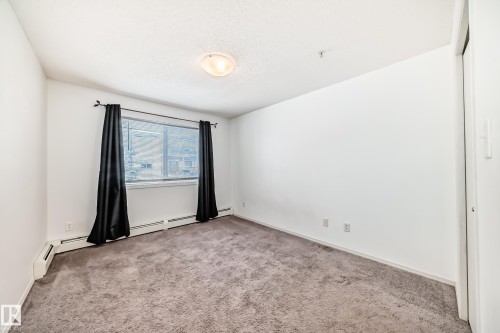Empty room featuring light carpet, a baseboard radiator, and a textured ceiling - 306 1188 Hyndman Road, Edmonton, AB - Indoor Photo Showing Other Room