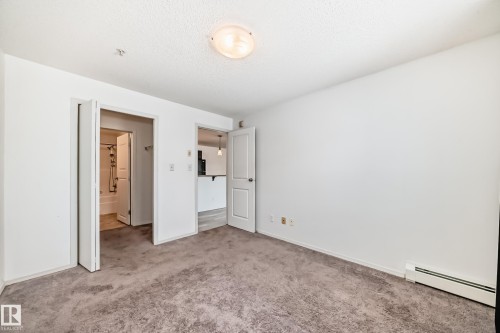 Unfurnished bedroom with a baseboard radiator, carpet floors, and a textured ceiling - 306 1188 Hyndman Road, Edmonton, AB - Indoor Photo Showing Other Room