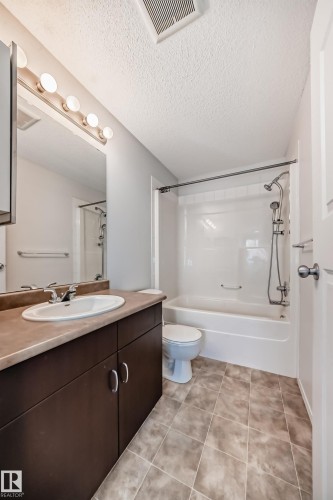 Bathroom featuring vanity, a textured ceiling, bathing tub / shower combination, and light tile patterned floors - 306 1188 Hyndman Road, Edmonton, AB - Indoor Photo Showing Bathroom