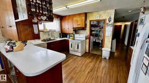 Kitchen with light countertops, a textured ceiling, white appliances, a peninsula, and wallpapered walls - 52012 Hwy 21, Rural Strathcona County, AB - Indoor Photo Showing Kitchen With Double Sink