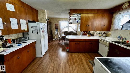 Kitchen featuring wallpapered walls, a peninsula, a textured ceiling, dark wood finished floors, and white appliances - 52012 Hwy 21, Rural Strathcona County, AB - Indoor Photo Showing Kitchen
