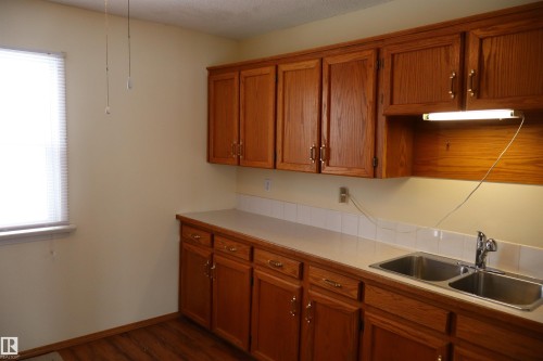 Kitchen with wood finish cabinets, light countertops, and dark wood-type flooring - 5109 55 Street, Barrhead, AB - Indoor Photo Showing Kitchen With Double Sink