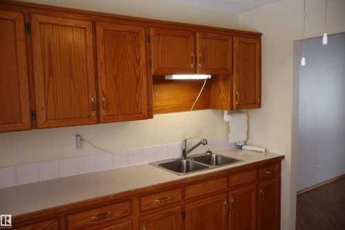 Kitchen featuring wood finish cabinets, light countertops, and decorative light fixtures - 5109 55 Street, Barrhead, AB - Indoor Photo Showing Kitchen With Double Sink