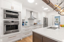 Kitchen with stainless steel appliances, light stone counters, light wood-type flooring, suspended lighting, and two tone cabinetry - 