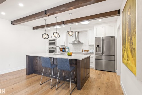 Kitchen featuring dual tone cabinetry, stainless steel fridge with ice dispenser, a kitchen breakfast bar, light wood-style flooring, and hanging light fixtures - 14412 80 Avenue Nw, Edmonton, AB - Indoor Photo Showing Kitchen With Upgraded Kitchen