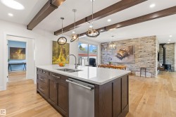Kitchen with dark wood finish cabinets, stainless steel dishwasher, light stone counters, light wood-style flooring, and an island with sink - 