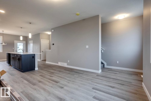 Kitchen with decorative light fixtures, a kitchen island with sink, light wood-type flooring, and light stone counters - 78 13139 205 Street Nw, Edmonton, AB - Indoor Photo Showing Kitchen