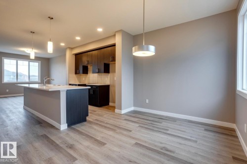 Kitchen with dark wood finish cabinetry, hanging light fixtures, a center island with sink, and light wood-style flooring - 78 13139 205 Street Nw, Edmonton, AB - Indoor Photo Showing Kitchen