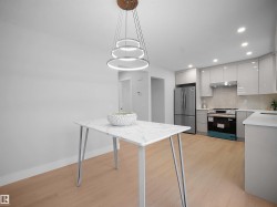 Kitchen with light wood finished floors, stainless steel appliances, hanging light fixtures, and backsplash - 