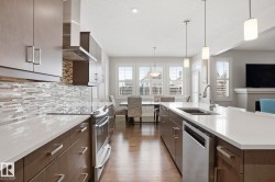 Kitchen with stainless steel appliances, dark wood finish cabinets, pendant lighting, light stone countertops, and a textured ceiling - 