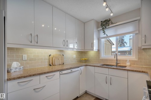 Kitchen featuring white cabinets, dishwasher, tasteful backsplash, a textured ceiling, and light stone counters - 7075 32 Avenue, Edmonton, AB - Indoor Photo Showing Kitchen With Double Sink