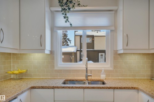 Kitchen view of light stone countertops, white cabinetry, and decorative backsplash - 7075 32 Avenue, Edmonton, AB - Indoor Photo Showing Kitchen With Double Sink