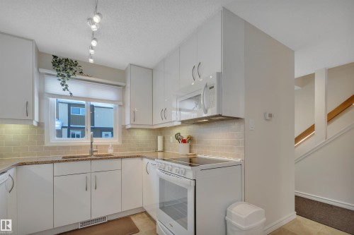 Kitchen featuring white appliances, white cabinetry, light stone countertops, and a textured ceiling - 7075 32 Avenue, Edmonton, AB - Indoor Photo Showing Kitchen