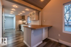 Kitchen with glass insert cabinets, white cabinets, a baseboard heating unit, a peninsula, and dark wood-type flooring - 