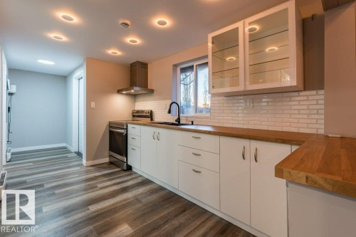 Kitchen with butcher block countertops, glass insert cabinets, white cabinetry, stainless steel range with electric cooktop, and tasteful backsplash - 4713 48 Avenue, Wetaskiwin, AB - Indoor Photo Showing Kitchen
