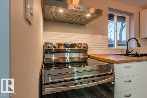 Kitchen featuring stainless steel range with electric stovetop, range hood, white cabinets, butcher block counters, and tasteful backsplash - 4713 48 Avenue, Wetaskiwin, AB - Indoor Photo Showing Other Room