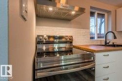 Kitchen featuring stainless steel range with electric stovetop, range hood, white cabinets, butcher block counters, and tasteful backsplash - 