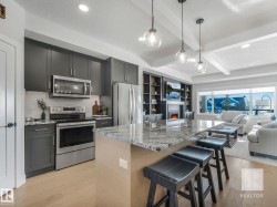 Kitchen featuring stainless steel appliances, light stone countertops, open floor plan, light wood-style floors, and hanging light fixtures - 