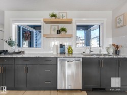 Kitchen with stainless steel dishwasher, light stone countertops, open shelves, light wood finished floors, and a textured ceiling - 