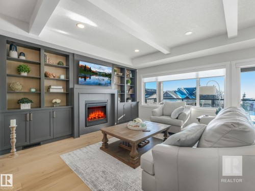 Living area featuring a textured ceiling, beam ceiling, light wood-type flooring, built in features, and a lit fireplace - 209 55101 Ste. Anne Trail, Rural Lac Ste. Anne County, AB - Indoor Photo Showing Living Room With Fireplace