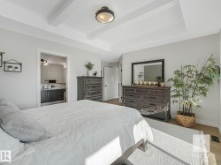Bedroom featuring connected bathroom, a tray ceiling, beamed ceiling, and wood finished floors - 