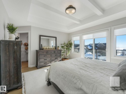 Bedroom featuring a spacious closet, access to outside, light wood finished floors, and a tray ceiling - 209 55101 Ste. Anne Trail, Rural Lac Ste. Anne County, AB - Indoor Photo Showing Bedroom