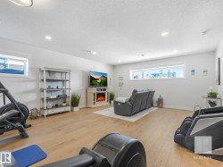 Workout room with light wood-type flooring, a lit fireplace, a textured ceiling, and recessed lighting - 