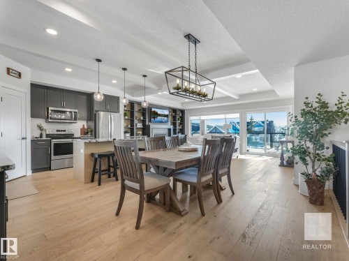 Dining space with a textured ceiling, light wood-style floors, suspended lighting, a fireplace, and beamed ceiling - 209 55101 Ste. Anne Trail, Rural Lac Ste. Anne County, AB - Indoor