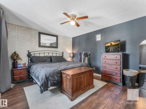 Bedroom with dark wood-style floors, brick wall, an accent wall, a ceiling fan, and a textured ceiling - 4504 48 Avenue, Onoway, AB - Indoor Photo Showing Bedroom