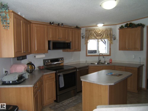 Kitchen with stainless steel appliances, a kitchen island, wood finish cabinetry, ornamental molding, and a textured ceiling - 125076 Twp Rd 540, Rural Two Hills County, AB - Indoor Photo Showing Kitchen With Double Sink