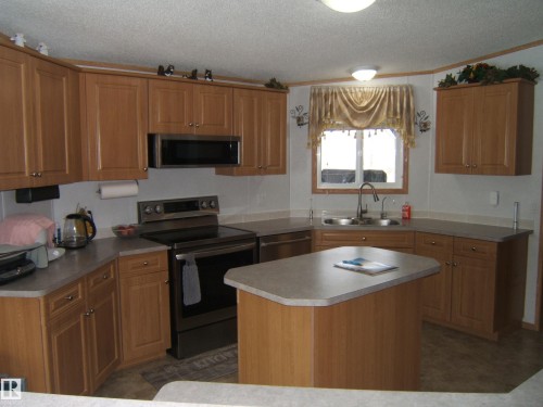Kitchen featuring stainless steel appliances, a kitchen island, wood finish cabinets, a textured ceiling, and crown molding - 125076 Twp Rd 540, Rural Two Hills County, AB - Indoor Photo Showing Kitchen With Double Sink
