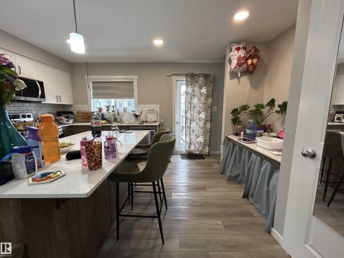 Kitchen with a breakfast bar, decorative backsplash, dark wood-style floors, and light stone counters - 120 1530 Tamarack Boulevard, Edmonton, AB - Indoor Photo Showing Dining Room