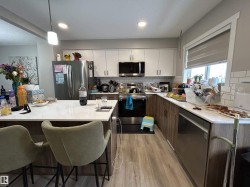 Kitchen featuring stainless steel appliances, a kitchen bar, backsplash, light wood finished floors, and light stone counters - 