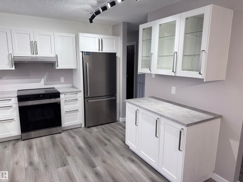 Kitchen with glass insert cabinets, white cabinetry, freestanding refrigerator, black range with electric cooktop, and a textured ceiling - 4919 49 Avenue, Vimy, AB - Indoor Photo Showing Kitchen