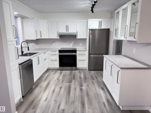 Kitchen with stainless steel appliances, white cabinetry, glass insert cabinets, a textured ceiling, and light countertops - 4919 49 Avenue, Vimy, AB - Indoor Photo Showing Kitchen