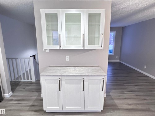 Bar featuring a textured ceiling, white cabinets, light wood-style flooring, and glass fronted cabinets - 4919 49 Avenue, Vimy, AB - Indoor Photo Showing Other Room