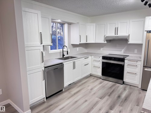 Kitchen with stainless steel appliances, a textured ceiling, white cabinetry, light wood-type flooring, and light stone countertops - 4919 49 Avenue, Vimy, AB - Indoor Photo Showing Kitchen