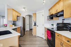Kitchen with stainless steel appliances, arched walkways, light wood finish cabinets, light stone counters, and rail lighting - 