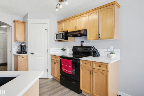 Kitchen featuring black / electric stove, light wood finish cabinets, light wood-type flooring, stainless steel microwave, and a textured ceiling - 4020 157A Avenue, Edmonton, AB - Indoor Photo Showing Kitchen