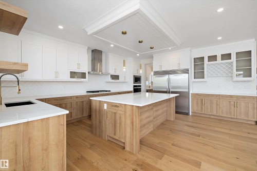 Kitchen with backsplash, built in appliances, light wood-style flooring, dual tone cabinets, and a kitchen island - 6871 Knox Loop Sw, Edmonton, AB - Indoor Photo Showing Kitchen With Upgraded Kitchen