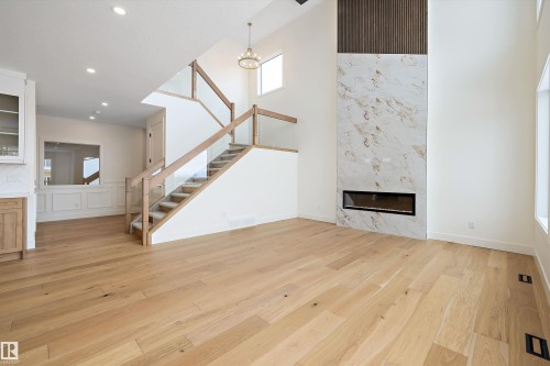 Unfurnished living room featuring a premium fireplace, light wood-style floors, a high ceiling, and recessed lighting - 6871 Knox Loop Sw, Edmonton, AB - Indoor With Fireplace