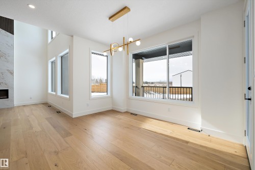 Unfurnished dining area featuring suspended lighting, a premium fireplace, and light wood-style flooring - 6871 Knox Loop Sw, Edmonton, AB - Indoor With Fireplace