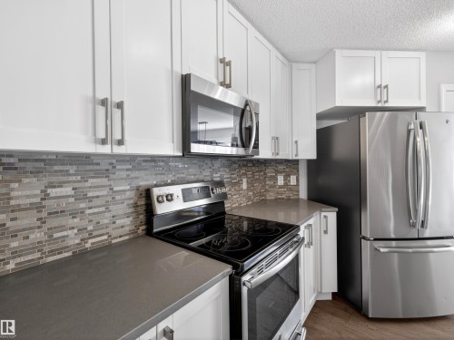 Kitchen with stainless steel appliances, white cabinetry, and a textured ceiling - 1267 Chappelle Boulevard, Edmonton, AB - Indoor Photo Showing Kitchen With Upgraded Kitchen