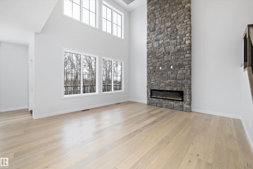 Unfurnished living room with a high ceiling, a stone fireplace, light wood finished floors, and healthy amount of natural light - 718 Elderberry Close Nw, Edmonton, AB - Indoor With Fireplace