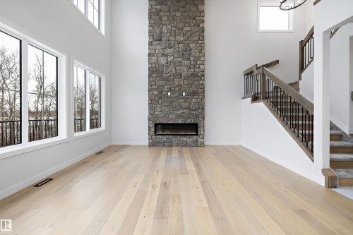 Unfurnished living room featuring a high ceiling, a fireplace, and light wood-style floors - 718 Elderberry Close Nw, Edmonton, AB - Indoor With Fireplace