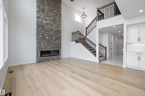 Unfurnished living room with a high ceiling, light wood-style floors, a stone fireplace, and a chandelier - 718 Elderberry Close Nw, Edmonton, AB - Indoor Photo Showing Other Room With Fireplace