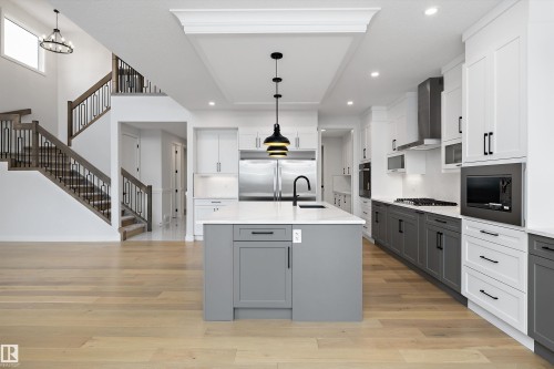 Kitchen with dual tone cabinets, light wood-style floors, light stone counters, built in appliances, and an island with sink - 718 Elderberry Close Nw, Edmonton, AB - Indoor Photo Showing Kitchen With Upgraded Kitchen