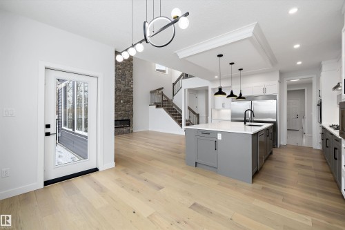 Kitchen with dual tone cabinetry, an island with sink, a fireplace, a chandelier, and light wood-style floors - 718 Elderberry Close Nw, Edmonton, AB - Indoor Photo Showing Kitchen With Upgraded Kitchen