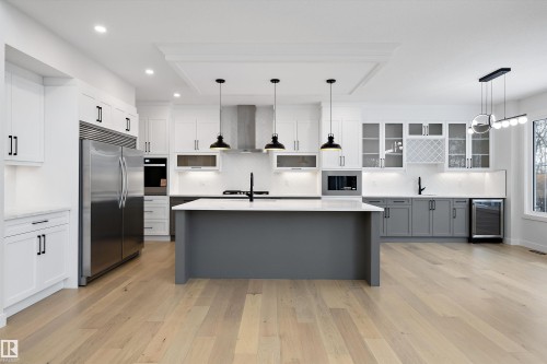 Two tone kitchen with stainless steel appliances, light stone countertops, a center island with sink, light wood finished floors, and dual tone cabinetry - 718 Elderberry Close Nw, Edmonton, AB - Indoor Photo Showing Kitchen With Upgraded Kitchen